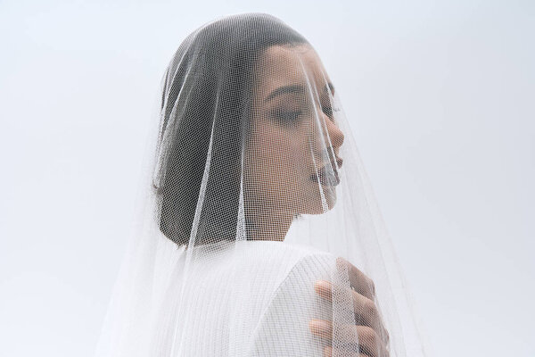 A radiant young bride stands delicately, draped in a fine veil, exuding grace and beauty.