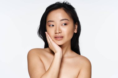 Genç Asyalı kadın yüzüne hafifçe dokunarak zarafet gösteriyor, kendine güven ve güzellik yayıyor..