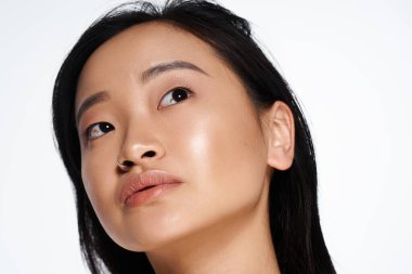 Genç Asyalı bir kadın, doğal güzelliğini ve özgüvenini göstererek düşünceli bir şekilde bakıyor..