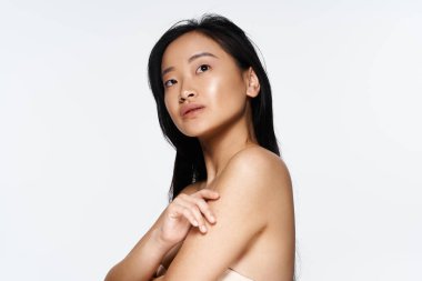 Genç Asyalı bir kadın basit bir arkaplana karşı zarif bir poz verir, ışıldayan güzellik ve duruş.