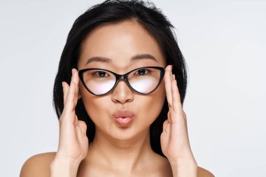 Parlak ışıklandırılmış stüdyo, genç Asyalı bir kadını elleri yüzlerinde şakacı bir şekilde poz verirken yakalıyor..