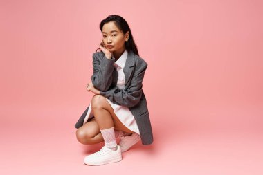 Modayı takip eden genç Asyalı bir kadın pembe bir stüdyoda şık kıyafetlerini sergiliyor..