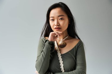 Genç bir Asyalı kadın minimalist bir stüdyoda düşünceli bir şekilde poz veriyor, stilini ve zarafetini ön plana çıkarıyor..