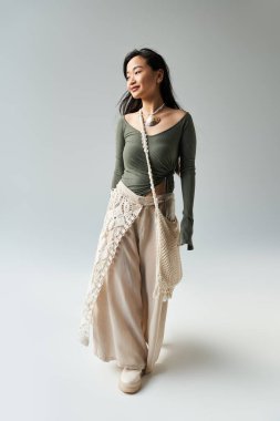 Genç Asyalı kadın, minimalist bir arkaplana karşı şık ve rahat bir şekilde dolaşır..