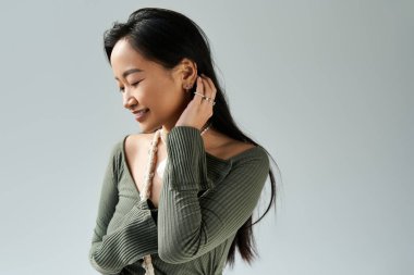 Işıl ışıl genç bir kadın nazikçe gülümser, evde otururken saçlarına sakin bir ifadeyle dokunur..