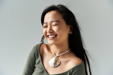 Neşeli, genç Asyalı kadın. Anın tadını çıkarıyor. Parlak ışıkta eşsiz kolyesini sergiliyor..