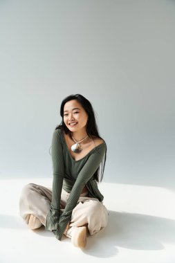 Genç bir Asyalı kadın sakin bir stüdyonun zemininde oturuyor, sıcaklık ve mutluluk saçıyor..