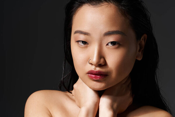 A stunning young Asian woman poses gracefully with her hands gently around her neck.