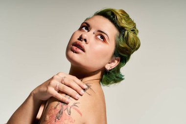 Genç bir kadın hayat dolu saç stiliyle ve dövmeleriyle hava atıyor. Kendine güveni tam..