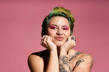 Kendine güvenen genç bir kadın neşeli poz verirken cesur makyaj ve şık dövmeler sergiliyor..