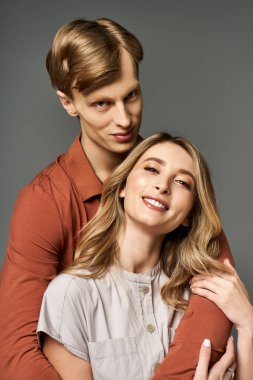 Genç bir çift stüdyoda poz veriyor, modaya uygun bahar kıyafetleri giyip neşeli ifadeler takınıyorlar..