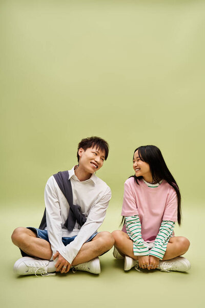 Charming couple enjoys each others company while sitting casually on a playful green backdrop.