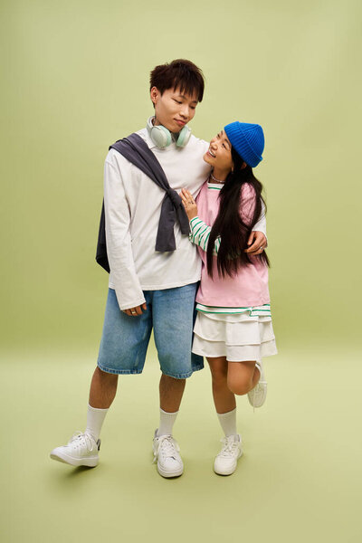 A stylish couple shares a playful moment, radiating love against a vivid green backdrop.