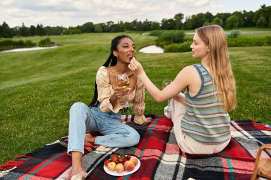 İki genç kadın piknik sırasında keyifli bir anı paylaşıyor. Lezzetli ikram ve içkilerin tadını çıkarıyorlar..