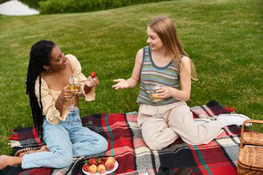 İki genç kadın neşeli bir pikniği paylaşıyor, gülüyorlar ve birbirlerine eşlik ediyorlar..