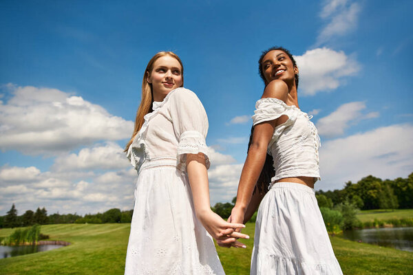 Two young women share a joyful moment in the park, holding hands and radiating happiness.