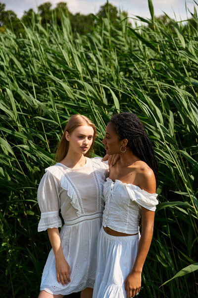 Two young women embrace each other in a verdant field, radiating love and happiness under the sun.