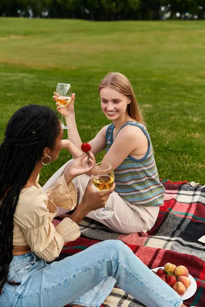 İki genç kadın, pikniğin tadını çıkarırken kahkahalarını paylaşıyor. Şarabın ve taze meyvenin tadını çıkarıyorlar..
