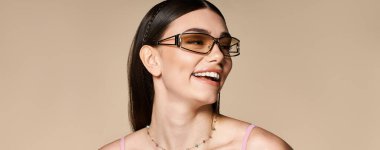 Güneş yanığı olan genç bir kadın parlak bir şekilde gülümser, yaz güneşinin altında şık güneş gözlüğünü gösterir, afiş