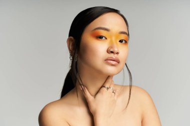 Parlak stüdyo, cesur turuncu makyajlı ve kendine güvenen genç Asyalı bir kadını sergiliyor..