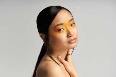 Genç bir Asyalı kadın zarif pozlar veriyor, canlı göz makyajını ve zarif tavırlarını vurguluyor..