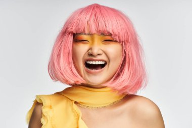 Pembe saçlı ve canlı makyajlı genç bir kadın modern bir stüdyoda neşeyle parlıyor..