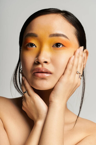 Красивая молодая азиатская женщина демонстрирует смелый желтый и оранжевый макияж глаз с выдержкой и изяществом.