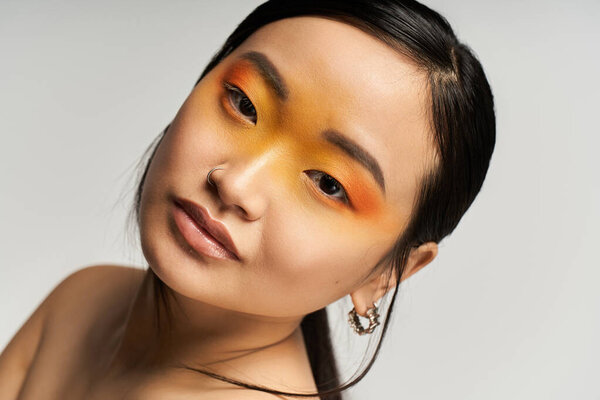 Яркий оранжевый макияж подчеркивает особенности молодой красивой азиатской женщины в шикарной студии.