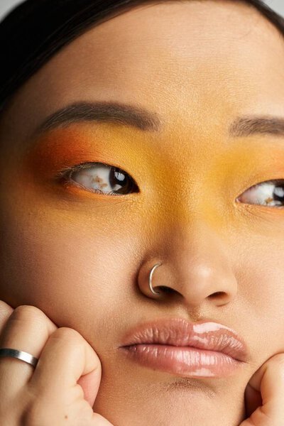 A young Asian woman with striking makeup showcases her emotions while posing thoughtfully, indoors.