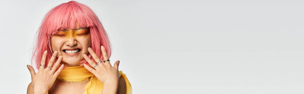 A joyful young Asian woman with pink hair and vibrant makeup radiates happiness.