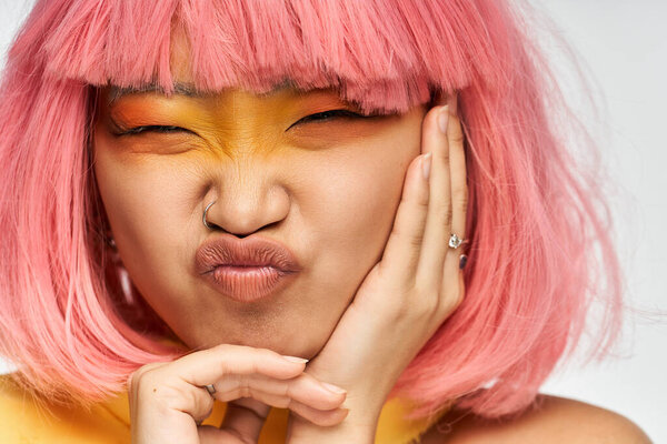 Cheerful young woman with pink hair poses playfully against a light background.