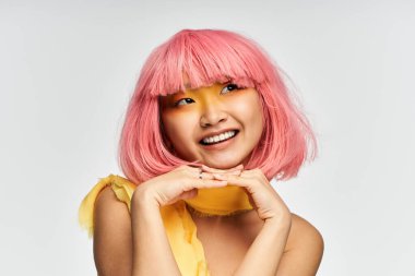 Pembe saçlı, yaratıcı, genç bir Asyalı kadın neşeli bir gülümseme ve neşeli bir poz veriyor..