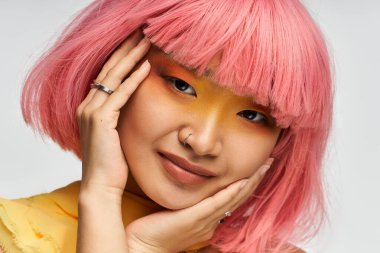 Neşeli, pembe saçlı, cesur makyajlı genç bir Asyalı kadın ışıldıyor..