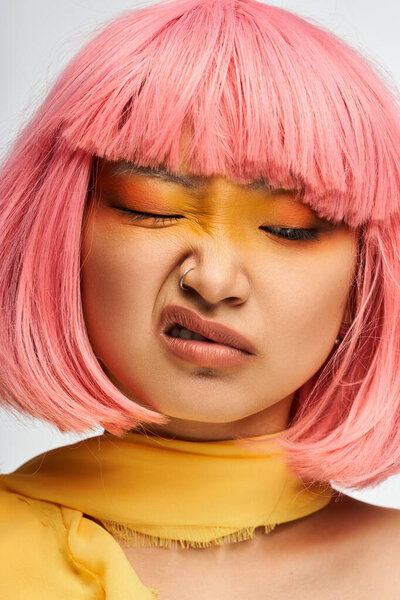 A young Asian woman showcases a unique expression, complementing her vibrant pink hair and makeup.