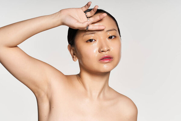A young Asian woman confidently shows off her radiant skin against a neutral backdrop.