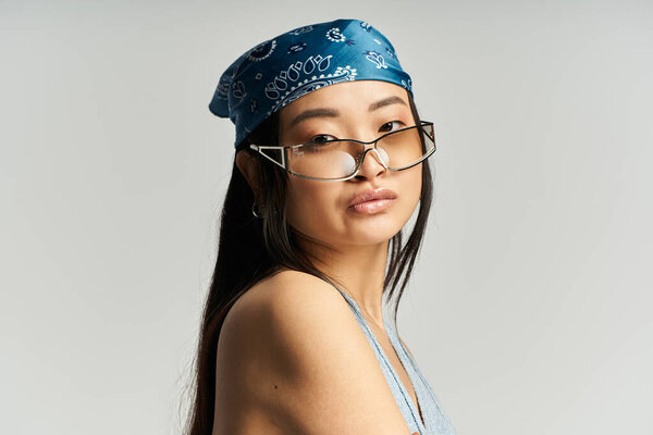 A young beautiful Asian woman wears a blue bandana and chic glasses, exuding confidence and charm.