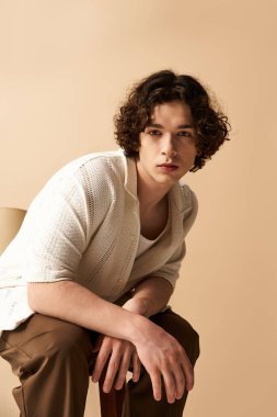 Kıvırcık saçlı genç adam şık yaz kıyafetleriyle minimalist bir stüdyo arkaplanına poz veriyor..