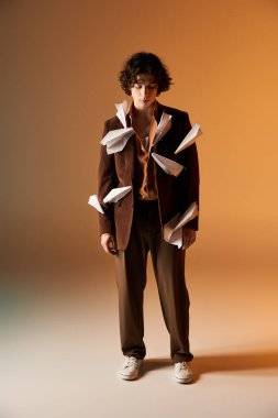 Kıvırcık saçlı genç bir adam stüdyoda kağıt uçaklar ve kahverengi kadife ceket giyiyor..