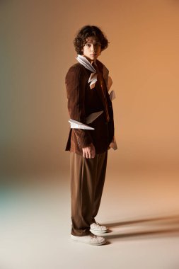 Kıvırcık saçlı genç bir adam ceketinde kağıt uçaklar olan şık bir görünüm sergiliyor..