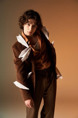 Kahverengi kadife ceketli genç bir kıvırcık adam stüdyo ortamında kağıt uçaklarla oynuyor..