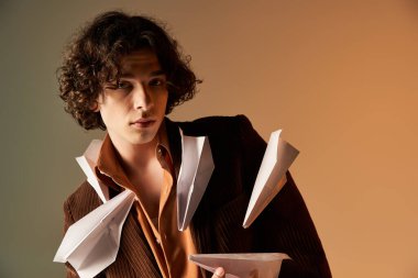 Stüdyoda, kıvırcık saçlı şık bir genç, kağıt uçaklarla süslenmiş bir spor ceketle poz veriyor..