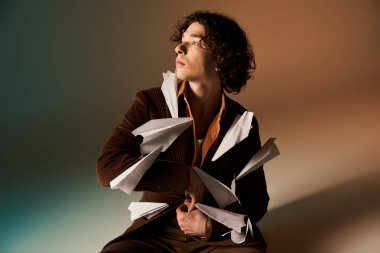 Kıvırcık saçlı genç bir adam şık bir kıyafet giymiş şık bir stüdyoda güven içinde poz veriyor..