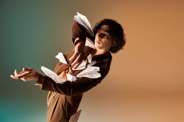 Canlı bir stüdyoda kıvırcık saçlı genç bir adam uçan kağıt uçaklarla tarzını sergiliyor..