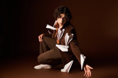 Genç adam stüdyoda yaratıcı bir poz veriyor, ceketi kağıt uçaklarla süslenmiş..