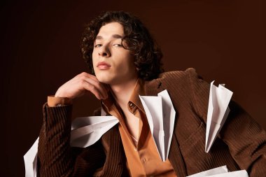 Yakışıklı bir genç, şık kıyafetlerini bir stüdyoda kağıt uçaklarla süslüyor..