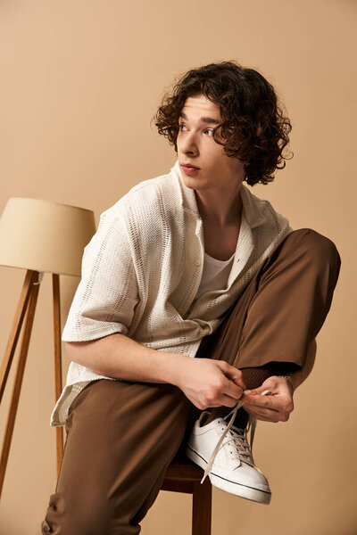 Curly-haired young man adjusting his stylish shoes in a chic studio environment.