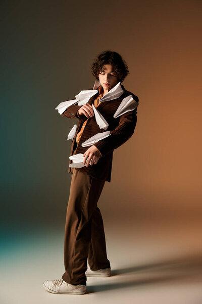 A stylishly dressed young man confidently shows off paper planes on his blazer in a modern studio.