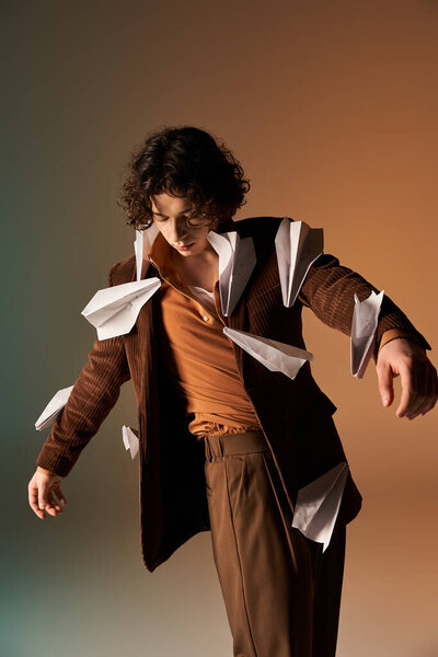 A young, stylish man with curly hair models a brown corduroy blazer adorned with paper planes.
