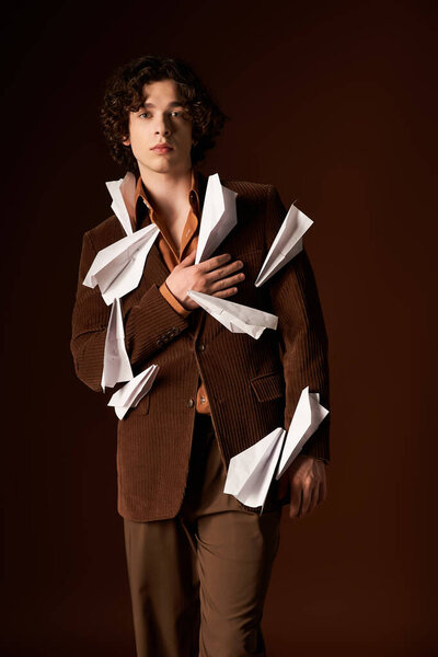 A confident young man in a brown corduroy blazer with paper planes poses strikingly in a studio.