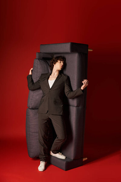 A good looking young man in black attire leans against furniture in a vibrant studio setting.